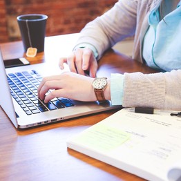 Eine junge Frau sitzt mit einem aufgeschlagenen Notizbuch neben ihrem Laptop und lernt